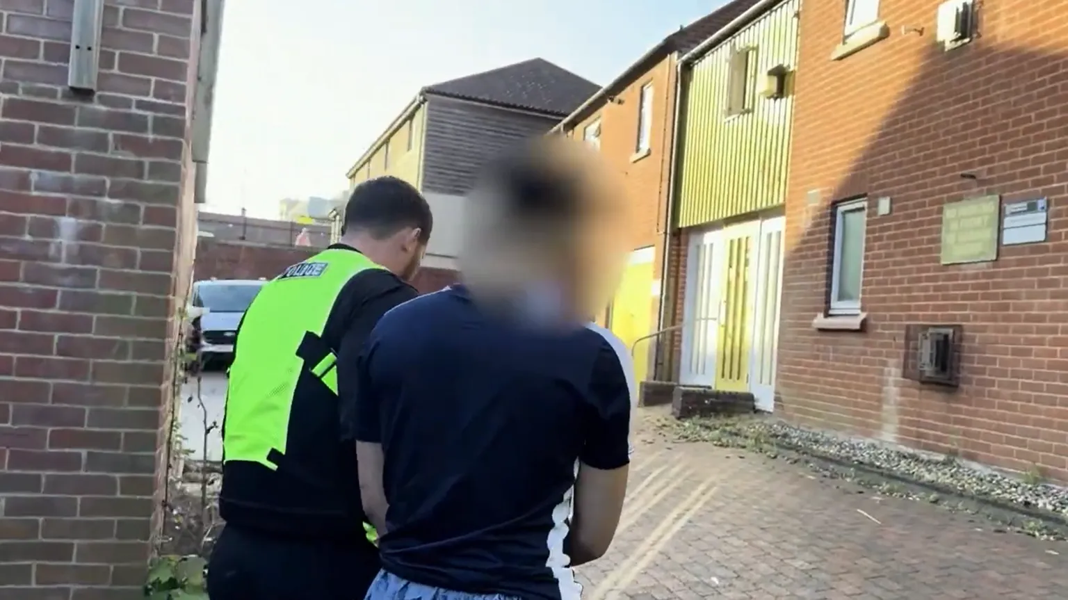 Norfolk Police Police officer in a high-visibility jacket accompanying a detainee following his arrest. 
